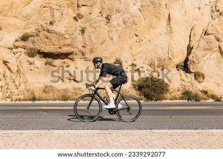 Side view of a professional cyclist in black sportswear riding bike at mountain