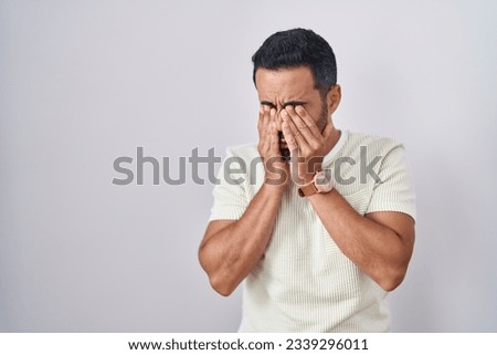 Hispanic man with beard standing over isolated background rubbing eyes for fatigue and headache, sleepy and tired expression. vision problem 