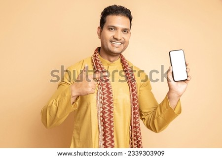 Happy young handsome indian man wearing traditional kurta holding smart phone with blank display screen isolated on beige background. Celebrate diwali festival, Wedding occasion groom, matrimony