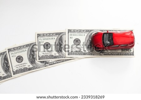 A close-up model of a beautiful sports car stands on a 100 American dollar bill isolated on a white background.