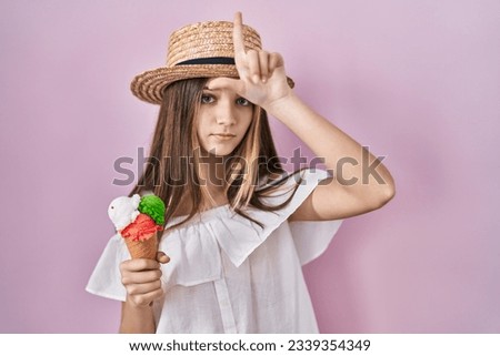 Teenager girl holding ice cream making fun of people with fingers on forehead doing loser gesture mocking and insulting. 