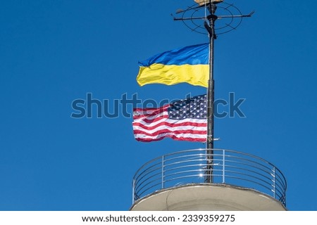 The flags of Ukraine and the USA flutter on a flagpole against a blue sky. State symbol. Ukrainian blue and yellow flag. Wind day outdoor.