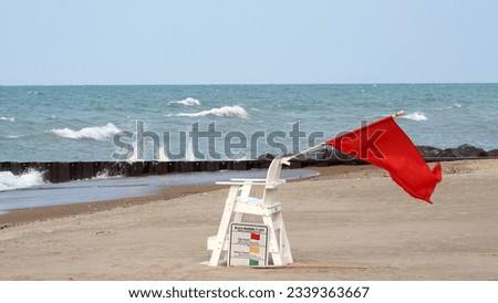 Red flag waves from a lifeguard chair as a warning during a closure at Kenilworth Beach on the Lake Michigan shore. Red flag is high hazard meaning high surf or strong currents.                    Royalty-Free Stock Photo #2339363667