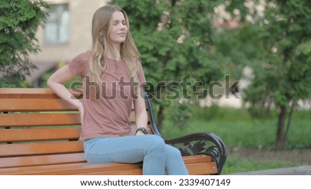 Young Woman with Back Pain Sitting Outdoor on a Bench Royalty-Free Stock Photo #2339407149