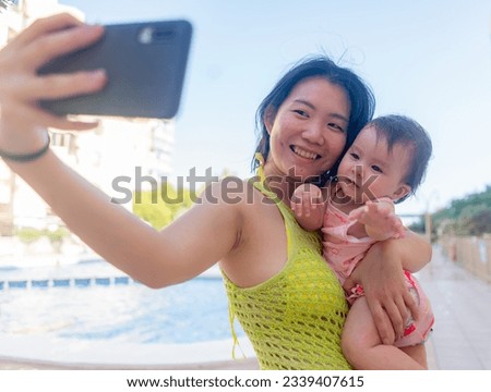 Asian woman taking selfie photo with her adorable baby girl - beautiful Korean mother holding her little daughter and taking picture with mobile phone during holidays