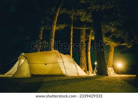 A white tent at night with stars in the sky among trees and grass in the nature and lights from lanterns in cozy vibes