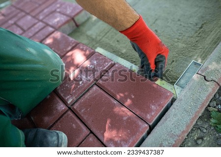 During the laying of paving blocks, the worker checks with a protractor, the correctness of the workmanship.