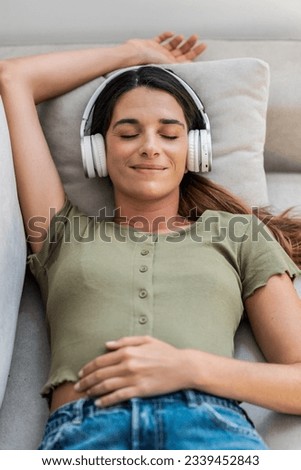 Shot of beautiful kind woman relaxing while listening music with headphones lying on couch at home