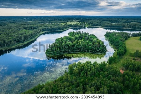 Aerial view of lake in Lithuania during summer season with sky reflections in water and lush green coastline and forest. Photo taken at lake Kumpuolis in north east part of Lithuania. Royalty-Free Stock Photo #2339454895