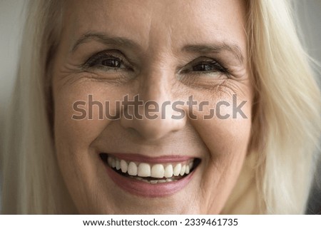 Facial portrait of happy cheerful elder woman with natural make up, wrinkles, healthy white teeth looking at camera with toothy smile, laughing. Blonde old senior lady close up shot