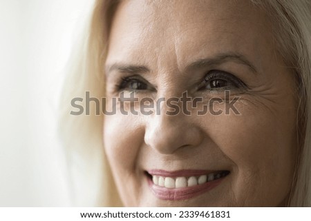Face of happy old retired woman with make up, looking away, smiling with perfect white teeth. Close up facial portrait of senior model promoting, beauty, dental care, eyesight