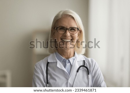 Happy positive mature doctor woman in white uniform head shot portrait. Medical professional, practitioner with stethoscope looking at camera with toothy smile, promoting healthcare consultation