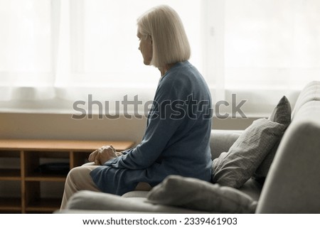 Lonely elderly retired woman sitting on sofa at home, feeling lost, depressed, stressed, apathy, going through health problems, loss, grief, suffering from memory loss, thinking on problems Royalty-Free Stock Photo #2339461903