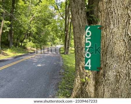 Close-up of a vertical green home address sign attached to an old tree trunk on a rural country road in the Pocono Mountains, Pennsylvania, USA