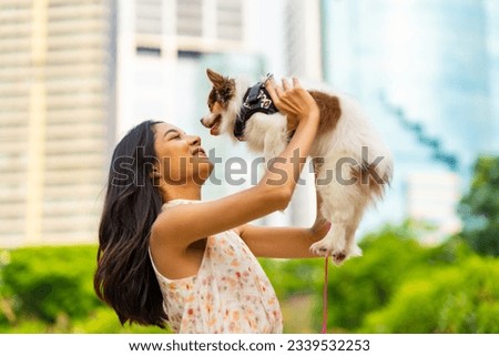 Asian woman playing with chihuahua dog at pets friendly dog park. Domestic dog with owner enjoy urban outdoor lifestyle in the city on summer vacation. Pet Humanization and urban pet parents concept.