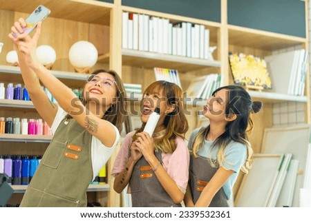 Group of Young Asian woman using mobile phone taking selfie together during learning acrylic painting workshop at art studio. University student artist enjoy and fun creating abstract modern art.