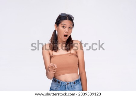 A young asian woman pointing at the camera, recognizing something or someone looking surprised and stunned. Isolated on a white background. Royalty-Free Stock Photo #2339539123