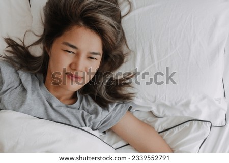 Top view of asian woman just wake up lying on the bed feeling not ready. High quality photo