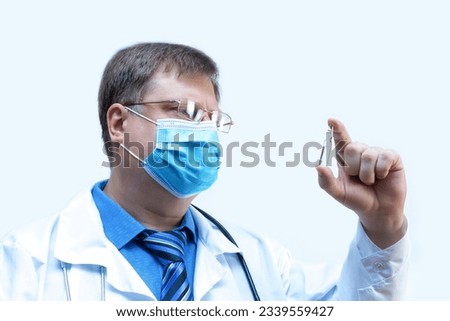 Male doctor looks at an ampoule with medicine vaccine, close-up white background.