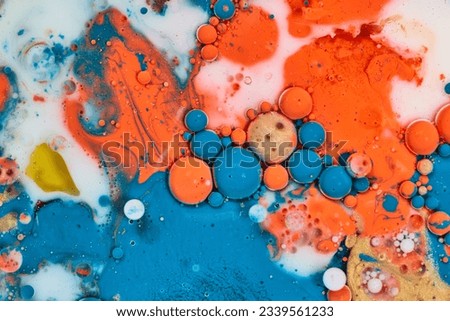 White milk with acrylic blue white yellow orange and gold paint poured on flat surface making a background asset