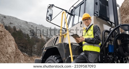 Engineer with tablet computer stands on the stairs to the cab of a truck Royalty-Free Stock Photo #2339587093