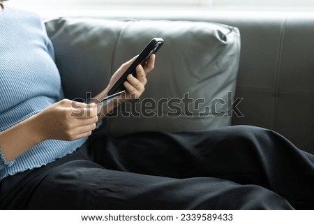 The girl used a credit card for online shopping on an Internet site on her smartphone while relaxing on the sofa at home. Remote Picture