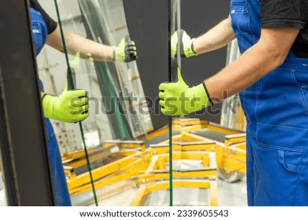 A glazier picks up sheets of thick glass from a rack in a glass factory, many mirrors cause mirror reflections Royalty-Free Stock Photo #2339605543