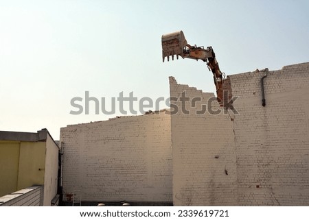 Demolition of a brick wall of an old building using an excavator bucket. Dismantling of the city's housing stock