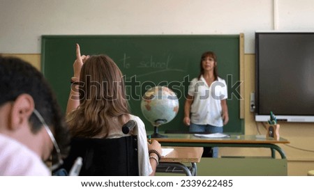 A pre-teen in a wheelchair raises her hand in a high school classroom. Back to school concept Royalty-Free Stock Photo #2339622485