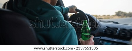 Drunk young man drives a car with a bottle of beer. This is a campaign picture of "Don't Drink for Drive."selective focus