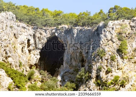 Cave or hollow. A large cave in the Oludeniz Fethiye part of the Taurus mountains. Natural formation. Forest, trees and blue sky. Horizontal photo. No people, nobody. Landscape.