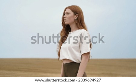 Beautiful Ginger Woman with magnificent Blue Eyes looking at Camera, touching her Red Hair. Attractive girl with nice Freckles smiling Charmingly at the Camera on Field. Natural Beauty. People. Royalty-Free Stock Photo #2339694927