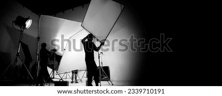 Silhouette of video production behind the scenes or B roll or making of TV commercial movie that film crew team lightman and cameraman working together with director in big studio with pro equipments