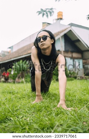 an Asian woman with sunglasses and a black shirt posing and crawling on the green grass