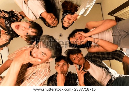 a group of Asian teenagers forming a circle and looking down with funny faces in an old room at night