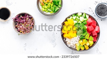 Poke bowl with raw tuna, avocado, sweet mango, cucumber, lettuce and white rice, soy sauce and sesame seeds. White table background, top view