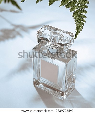 Transparent glass perfume bottle with light shadows on gray. No name bottle for representation. Trending concept with green plant. Women's and men's essence. Minimal style perfumery template