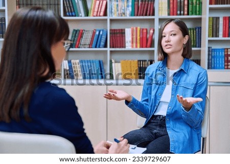 Female student talking with mentor psychologist in office with bookshelves Royalty-Free Stock Photo #2339729607