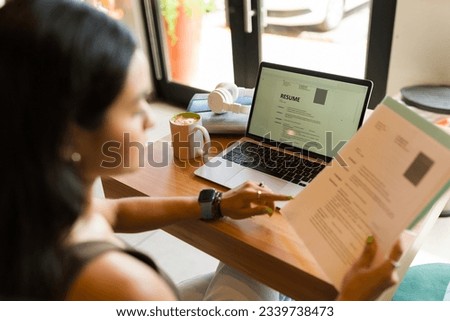 Young woman looking for a new job and sending her online CV resume using the internet zone of the coffee shop Royalty-Free Stock Photo #2339738473