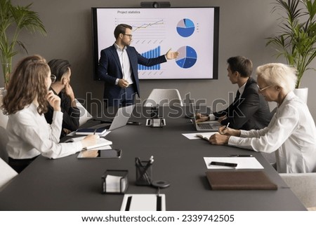 Confident young business leader man presenting marketing statistic report to partners, investors, selling startup project on meeting, negotiations, showing graphs on electronic display