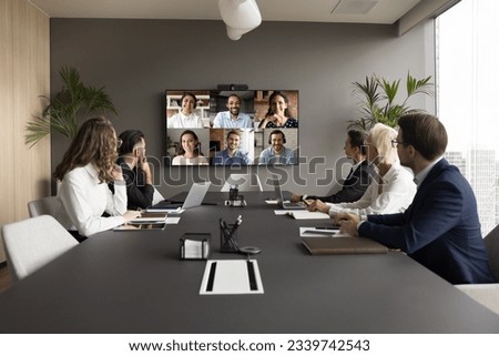 Office staff meeting with diverse freelance team on online video conference, making group call on internet, sitting at table looking at electronic board with head shots, discussing work project Royalty-Free Stock Photo #2339742543