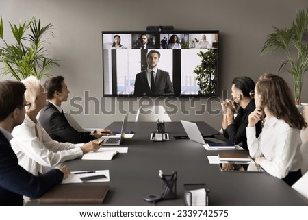 Business team and leader meeting online and offline, sitting at conference table, looking at interactive board with headshots, listening to speaker, CEO, discussing project on group video call Royalty-Free Stock Photo #2339742575