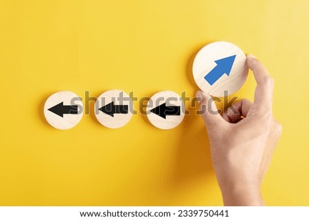 Hand holding Blue arrow and different direction facing opposite direction with black arrow for business disruption and technology transformation and different thinking idea concept