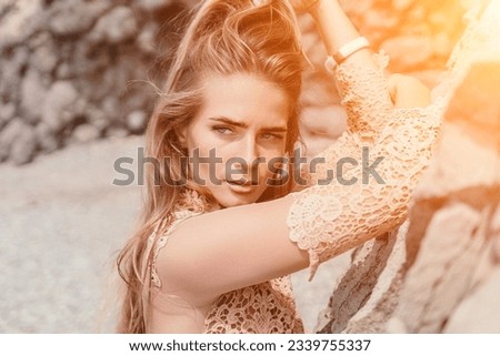Woman summer travel sea. Happy tourist in beige dress enjoy taking picture outdoors for memories. Woman traveler posing on the beach surrounded by volcanic mountains, sharing travel adventure journey