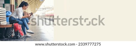 Banner of Cheap Travel and Lifestyle concept. Holiday Time, Young Solo Traveler woman wearing jean and sitting at train station. Asian Backpacker waiting train alone and using smartphone to  plan trip
