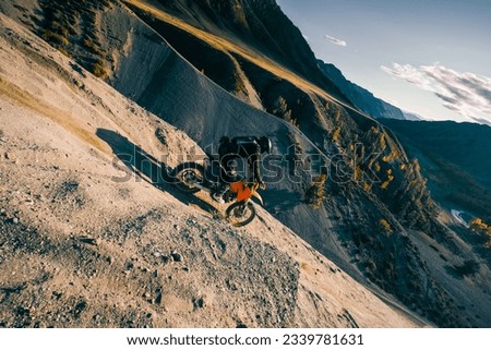 Extreme Rider climbing sand mountain top on off-road cross enduro motorcycle. Beautiful mountains landscape down on background, colourful autumn forest and river in sunshine Royalty-Free Stock Photo #2339781631