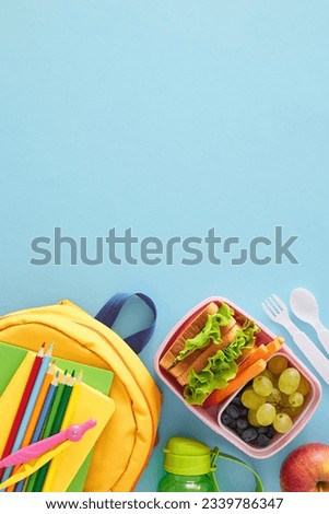 Healthy snack choice for school. Top view vertical photo of lunchbox with sandwiches, snacks, water bottle, compass, pencils, copybook, cutlery on pastel blue background with space for advert or text Royalty-Free Stock Photo #2339786347