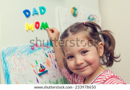 child forming mom and dad words with magnetic letters on refrigerator door.