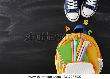 Stepping into the world of education. Top view photo of stylish schoolbag, sneakers, notebook, compass, pens, marker, letters on blackboard with empty space for promo or text
