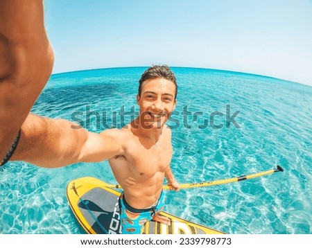 One happy caucasian man enjoying and having fun in vacations outdoors in the beach riding a paddle surf in the water. Attractive boy feeling free traveling.